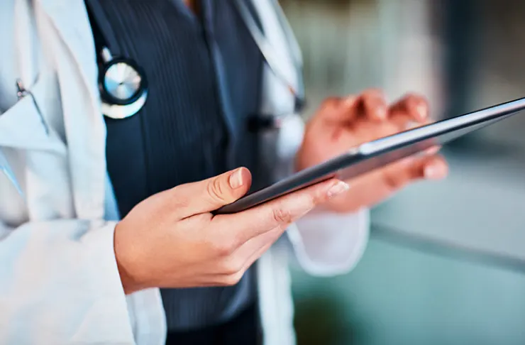 A person in a white lab coat with a stethoscope is holding and interacting with a tablet device.