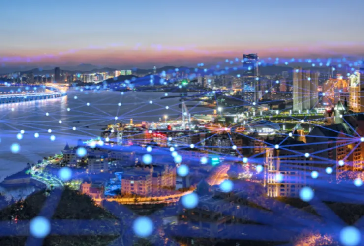 Cityscape at dusk with illuminated buildings and waterfront. Overlay of interconnected blue dots and lines suggests digital connectivity and technology network.