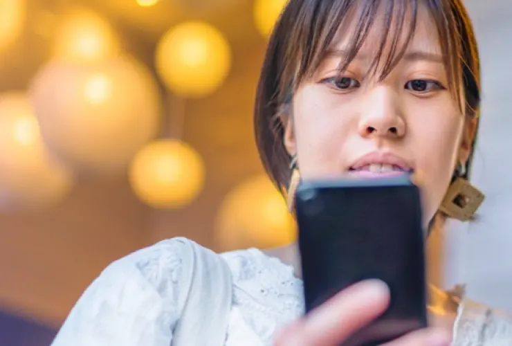 Person looking down at a smartphone, with blurred spherical lights in the background.