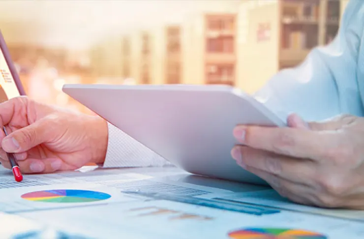 Person holding a tablet and using a pen to take notes on documents with charts and graphs.