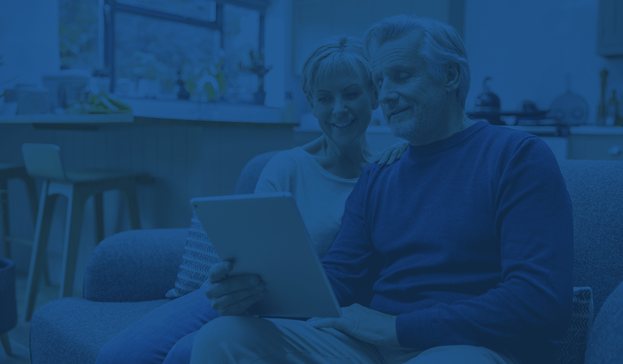 A man and woman are seated on a couch, both engaged with a tablet in their hands