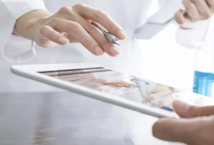 Close-up of two individuals wearing lab coats, one pointing at a tablet screen with a pen, suggesting a discussion or review of information.