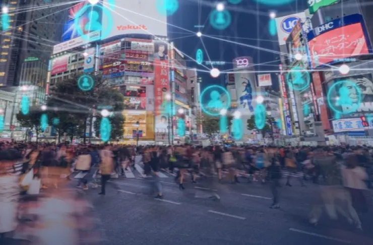 Crowded city street intersection with digital icons and connections superimposed, depicting network connectivity and social interaction among people. Illuminated billboards and signs in background.