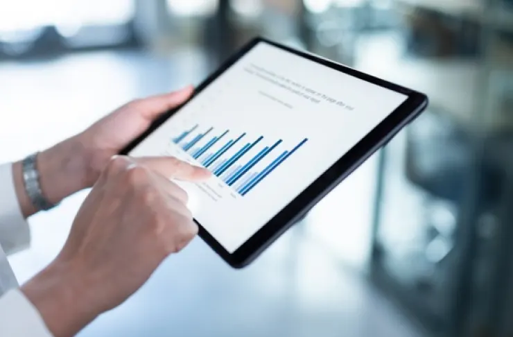 A person uses a tablet displaying a bar graph with blue bars, analyzing data and information.