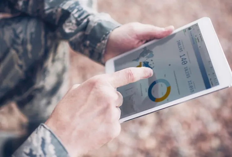 Person in military uniform using a tablet displaying data charts and statistics.