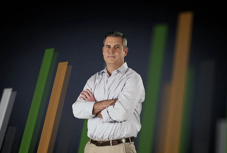 A man in a light gray shirt smiles in front of a dark background with green connected dots.