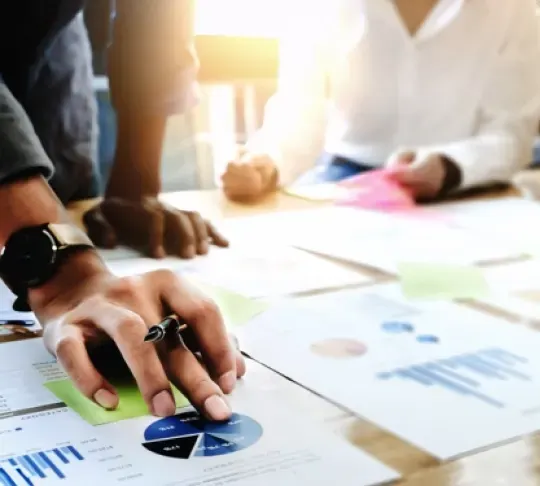 Close-up of hands and documents on a table, showing charts and graphs during a meeting.