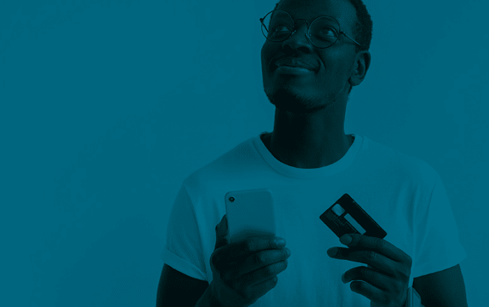 A person wearing glasses holds a smartphone in one hand and a credit card in the other, looking up thoughtfully against a blue background.