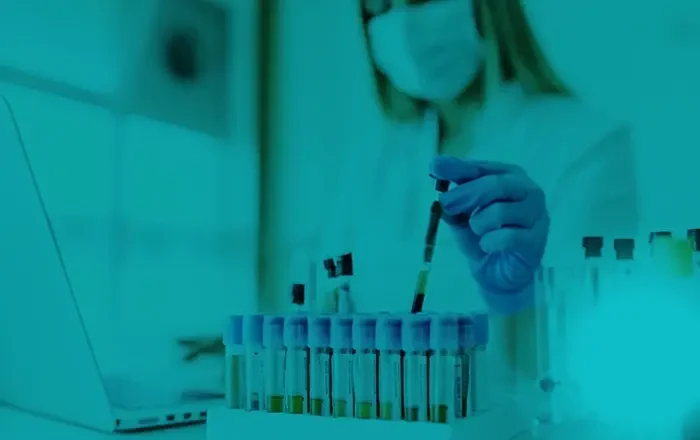 A scientist wearing a mask and gloves is conducting a test with a pipette and test tubes in a laboratory.