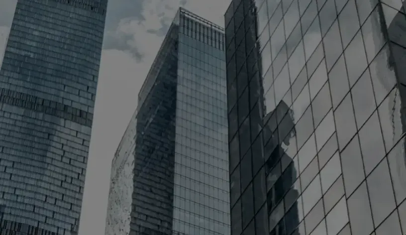 Skyscrapers with glass facades reflecting neighboring buildings under a cloudy sky in a metropolitan financial district.