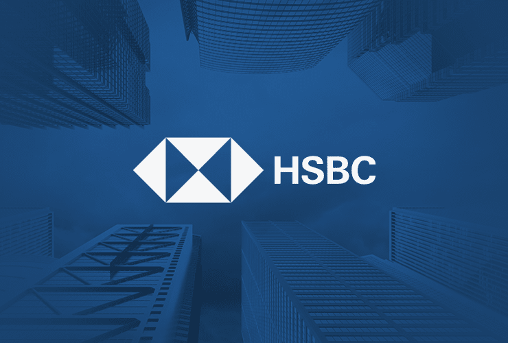 HSBC logo in white set against a blue background, surrounded by tall skyscrapers seen from a low angle looking up.