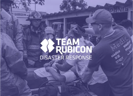 Team Rubicon members and emergency responders assist an injured individual on a stretcher, with "Team Rubicon Disaster Response" text overlaying the image.