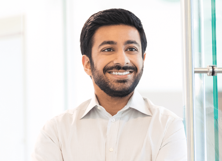 Headshot of Qlik Board of Directors member, Mohnish Gandhi. He has short dark hair and beard, is wearing a light-colored dress shirt, and smiles while standing with arms crossed.