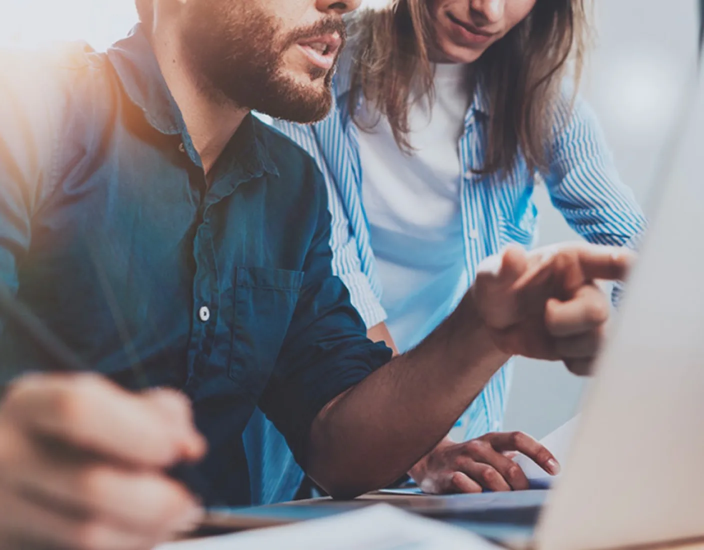 Two people are collaborating while looking at a laptop. One person is pointing at the screen, discussing the content they are viewing.