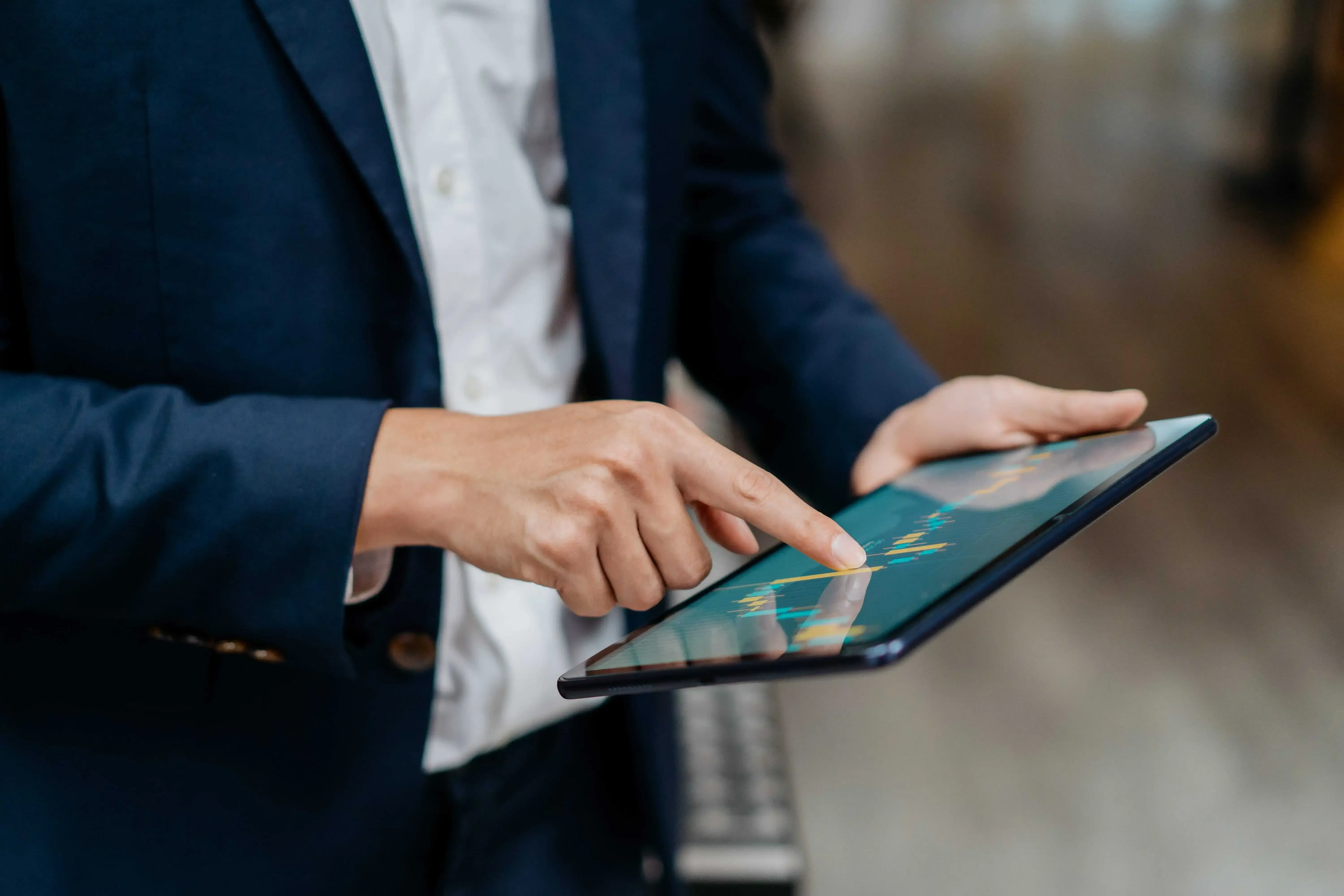 A person in a blue suit uses a tablet computer, focusing on a chart displayed on the screen.