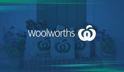 Woolworths logo on a blue background with shopping bags filled with groceries, flanked by potted plants.