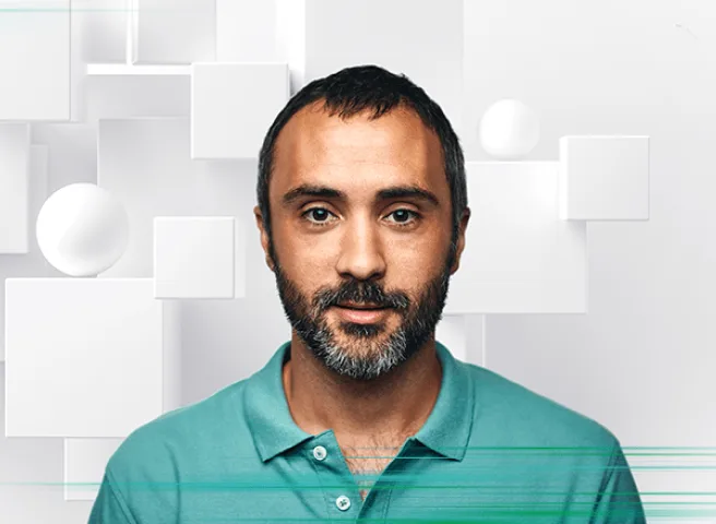 A man with a short beard and a turquoise polo shirt stands against a modern, geometric white background.