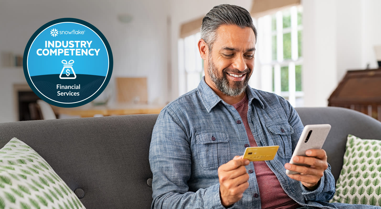 A man sits on a couch, holding a credit card and a smartphone. Overlayed next to him is a badge that reads "Snowflake Industry Competency: Financial Services".